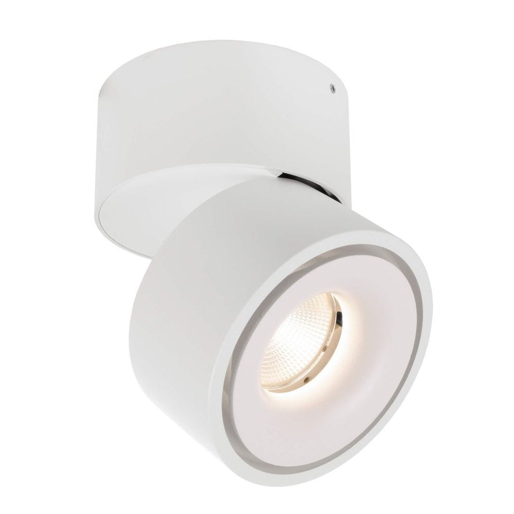 Spot blanc orientable fixé au plafond, tête cylindrique inclinée et lumière allumée.