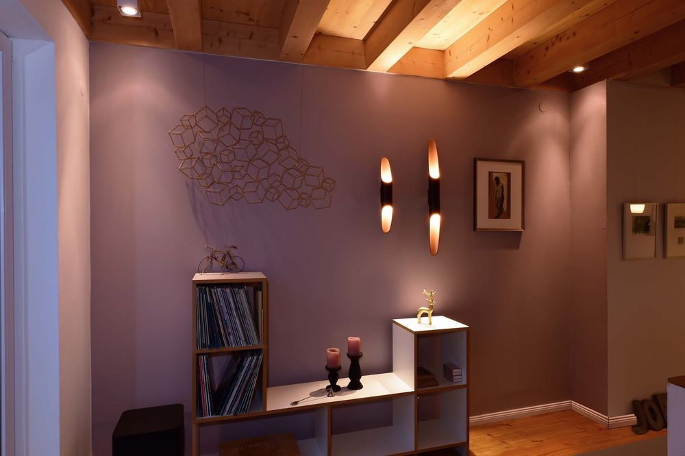 Mise en ambiance sur mur violet, deux appliques allumées au-dessus d'un meuble.