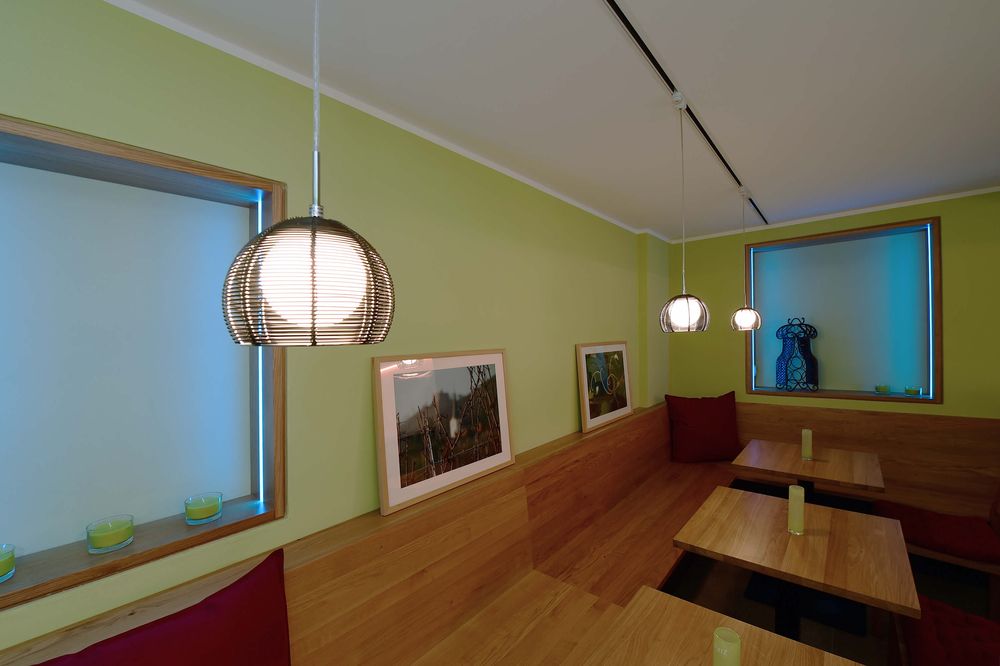 Trois suspensions allumées au-dessus de tables en bois dans un café vert