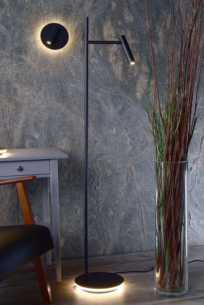 Lampadaire noir allumé dans un salon, près d’un vase et d’une table grise