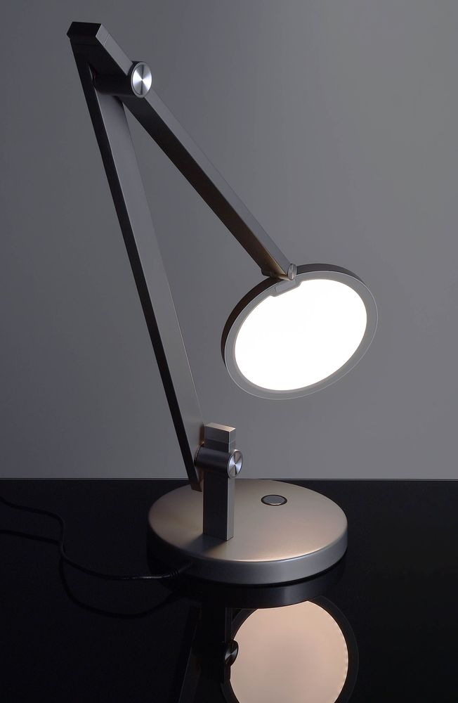 Lampe allumée sur surface noire réfléchissante, montrant l'abat-jour rond et le bras incliné