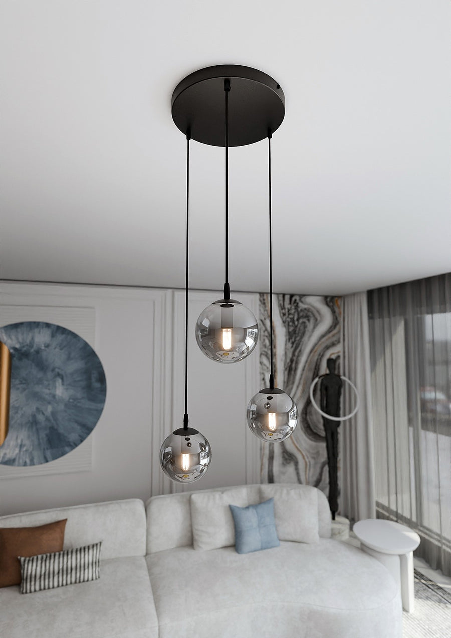 Suspension noire à trois globes transparents installée au-dessus d’un canapé blanc