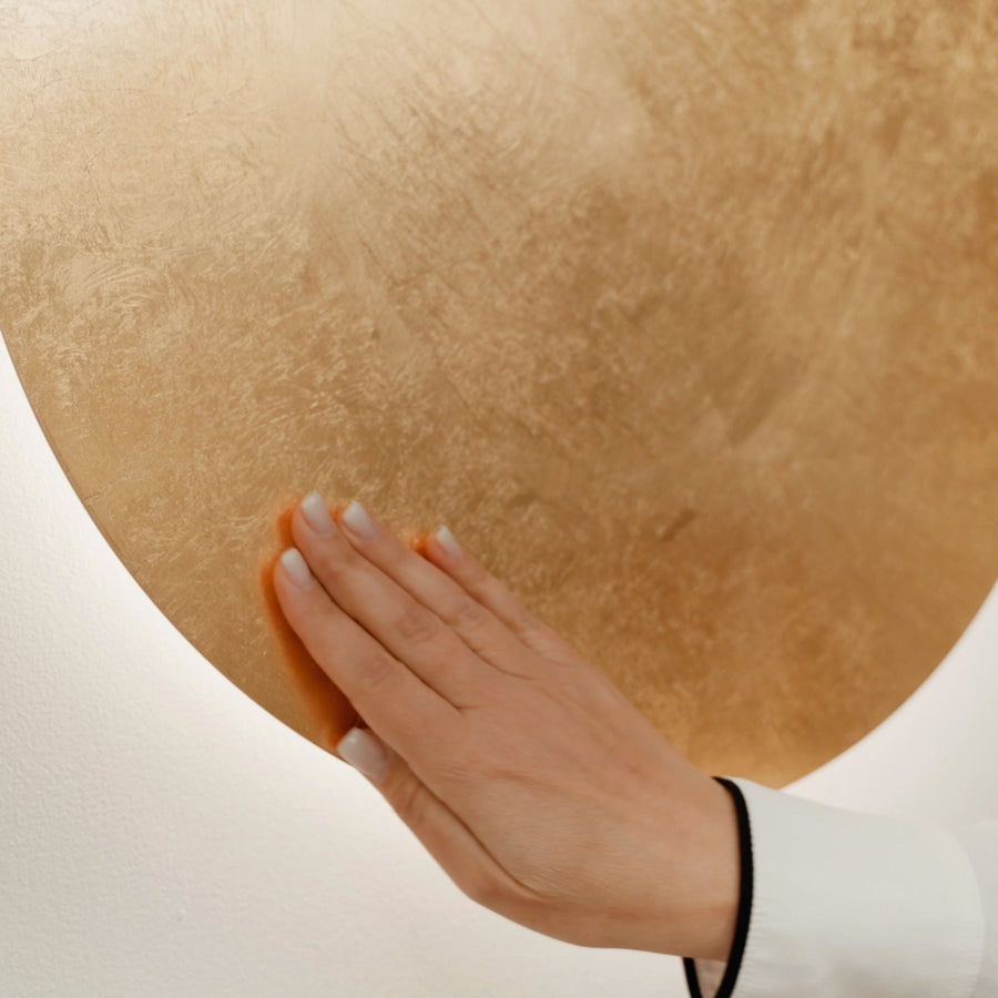 Main caressant la surface texturée en feuille d'or d'un disque lumineux.