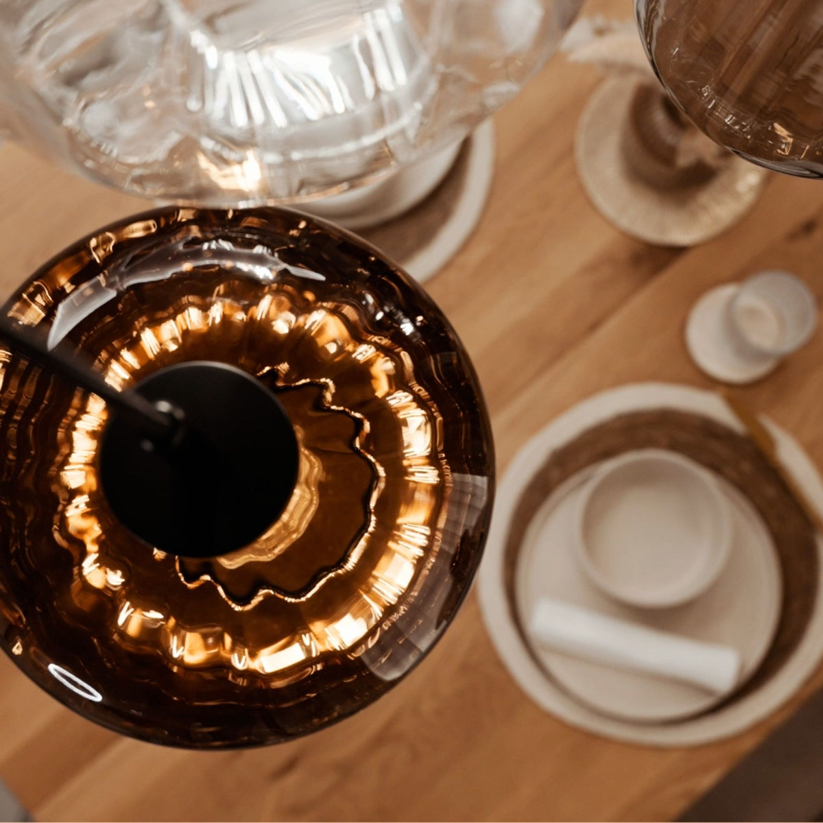 Vue du dessus d'une suspension en verre ambré au-dessus d'une table dressée avec assiettes.