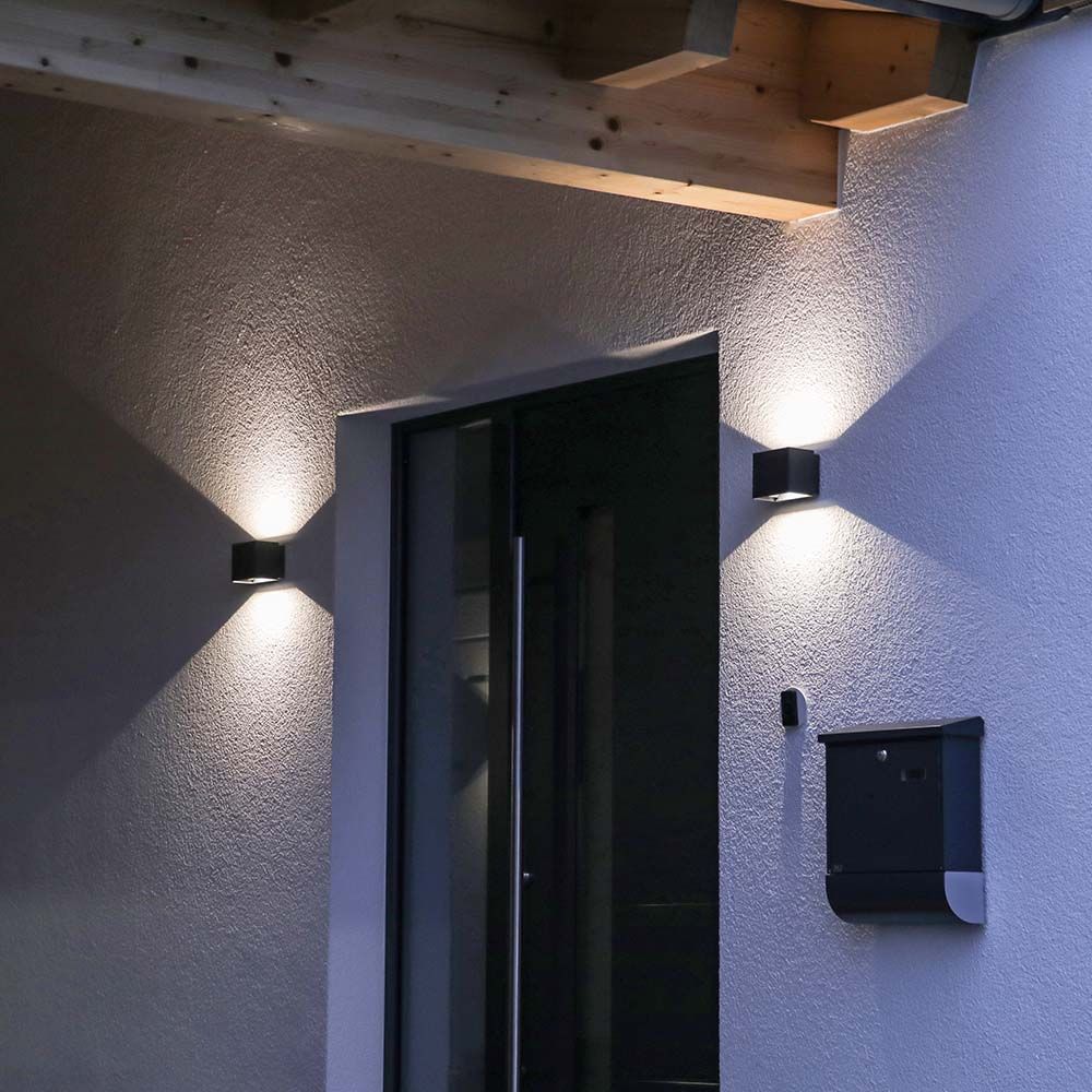 Entrée extérieure de nuit, appliques sombres de part et d'autre d'une porte vitrée.