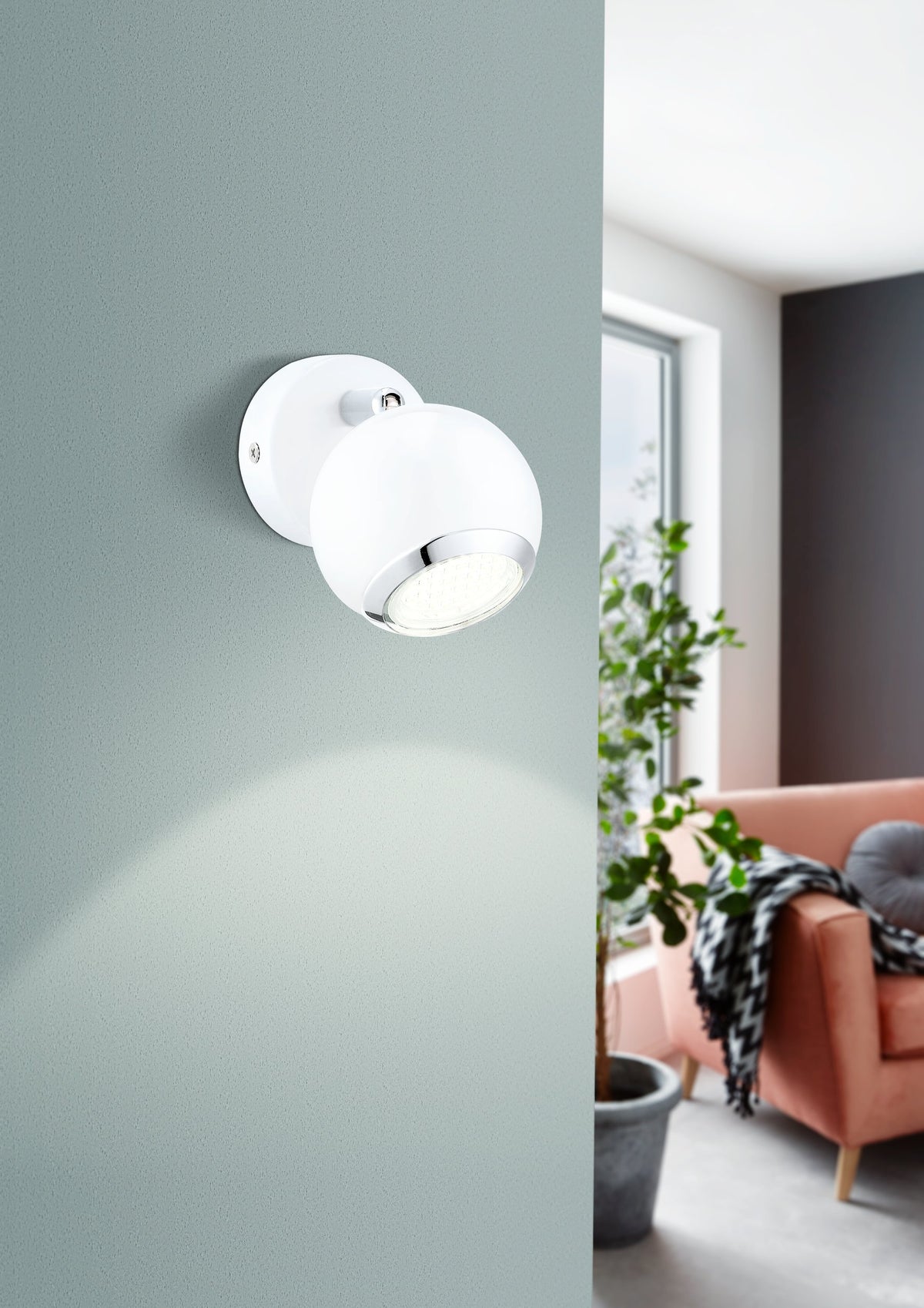 Applique murale installée sur un mur gris clair dans un salon avec canapé et plante.