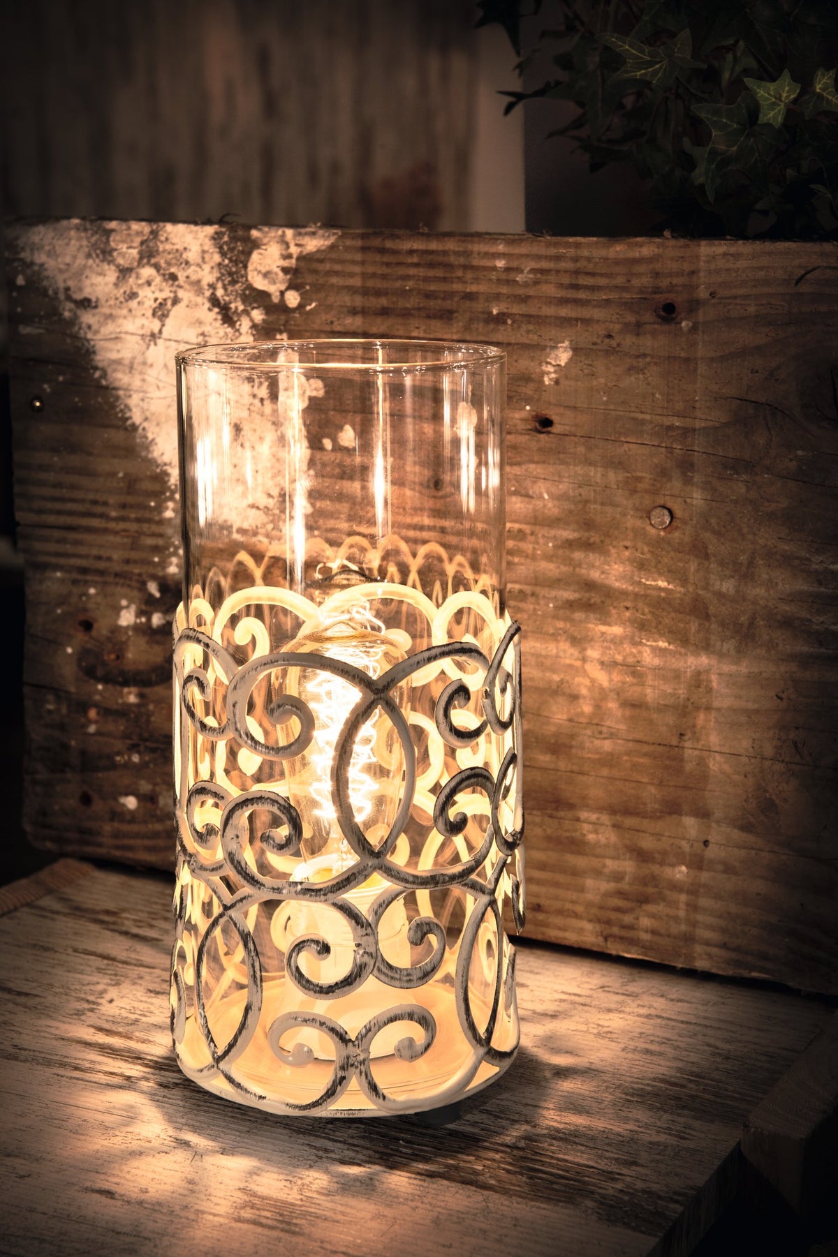 Gros plan de la lampe allumée sur bois rustique, lumière chaude et feuillage sombre