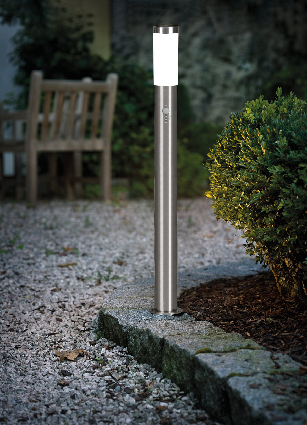 Lampadaire allumé éclairant une allée de gravier près d'un arbuste