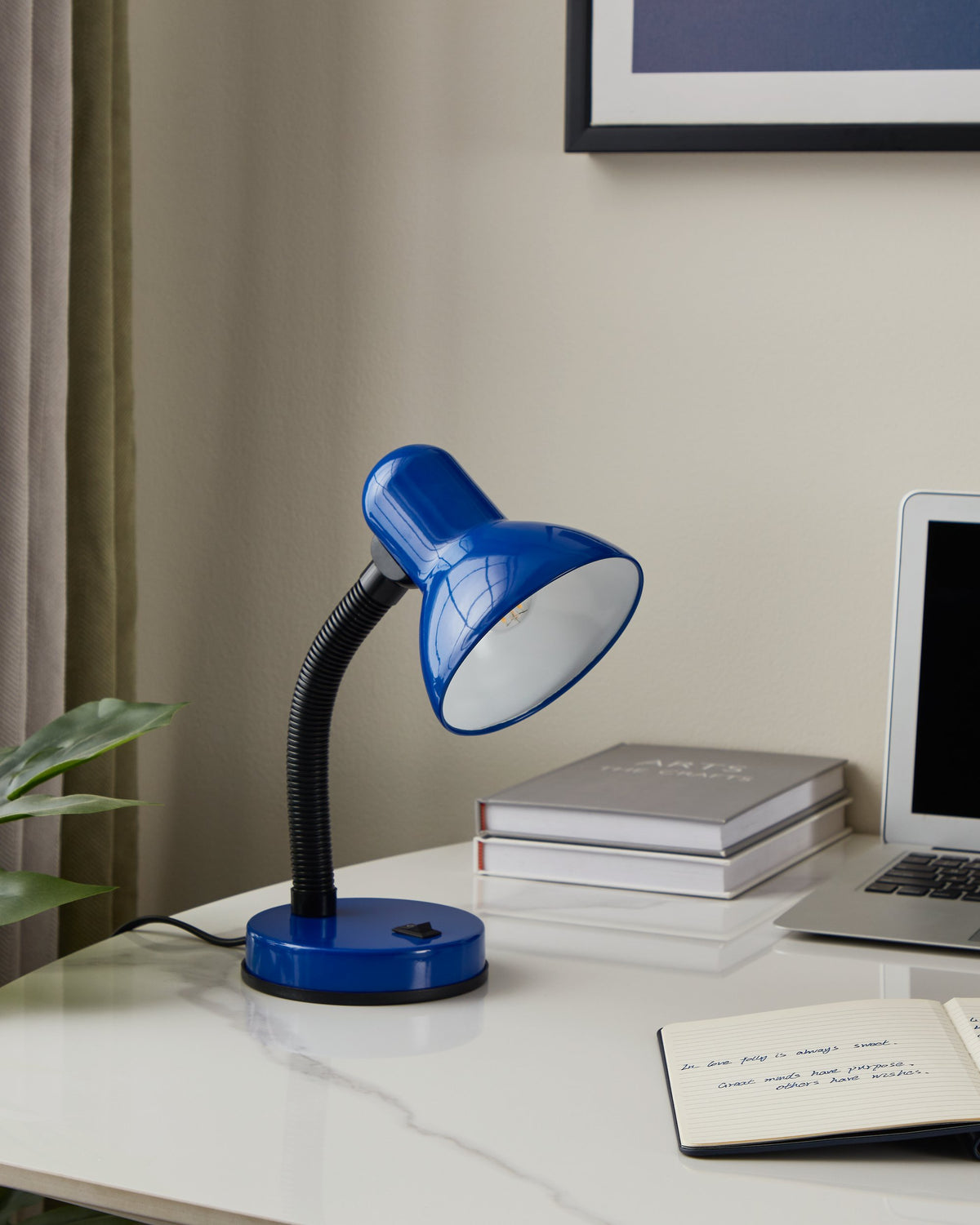 Lampe bleue posée sur un bureau avec ordinateur portable, carnet et plante.