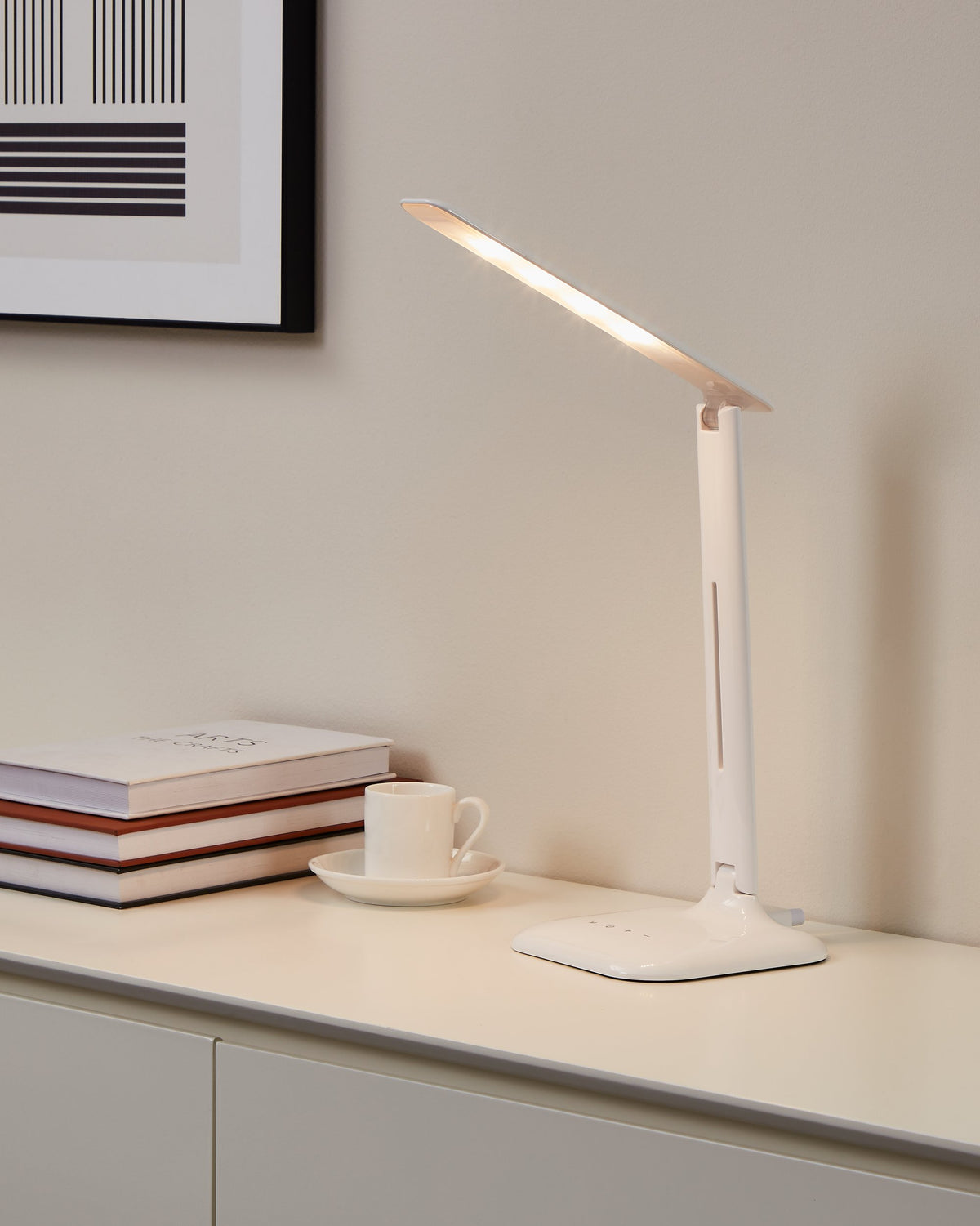 Mise en ambiance sur un meuble blanc, lampe allumée près de livres et d'une tasse.
