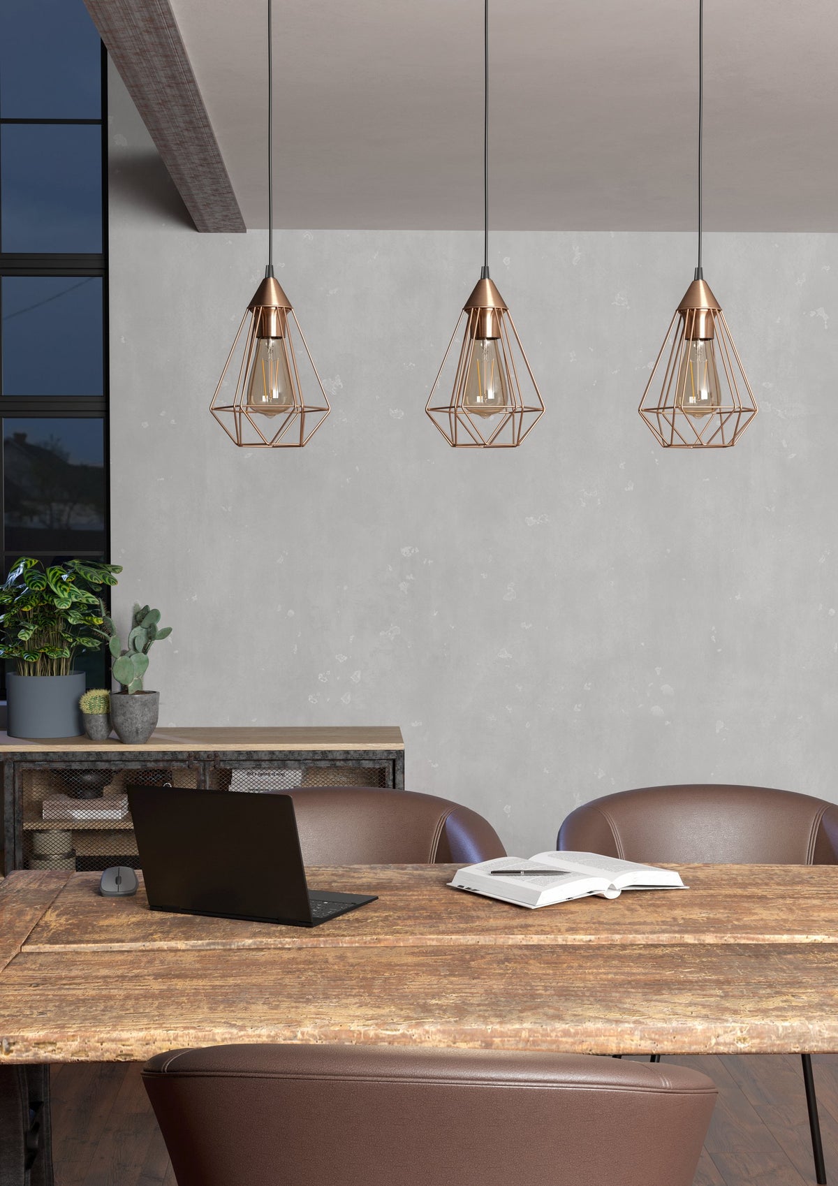Ambiance bureau avec trois suspensions cuivrées éclairant une table en bois et un ordinateur