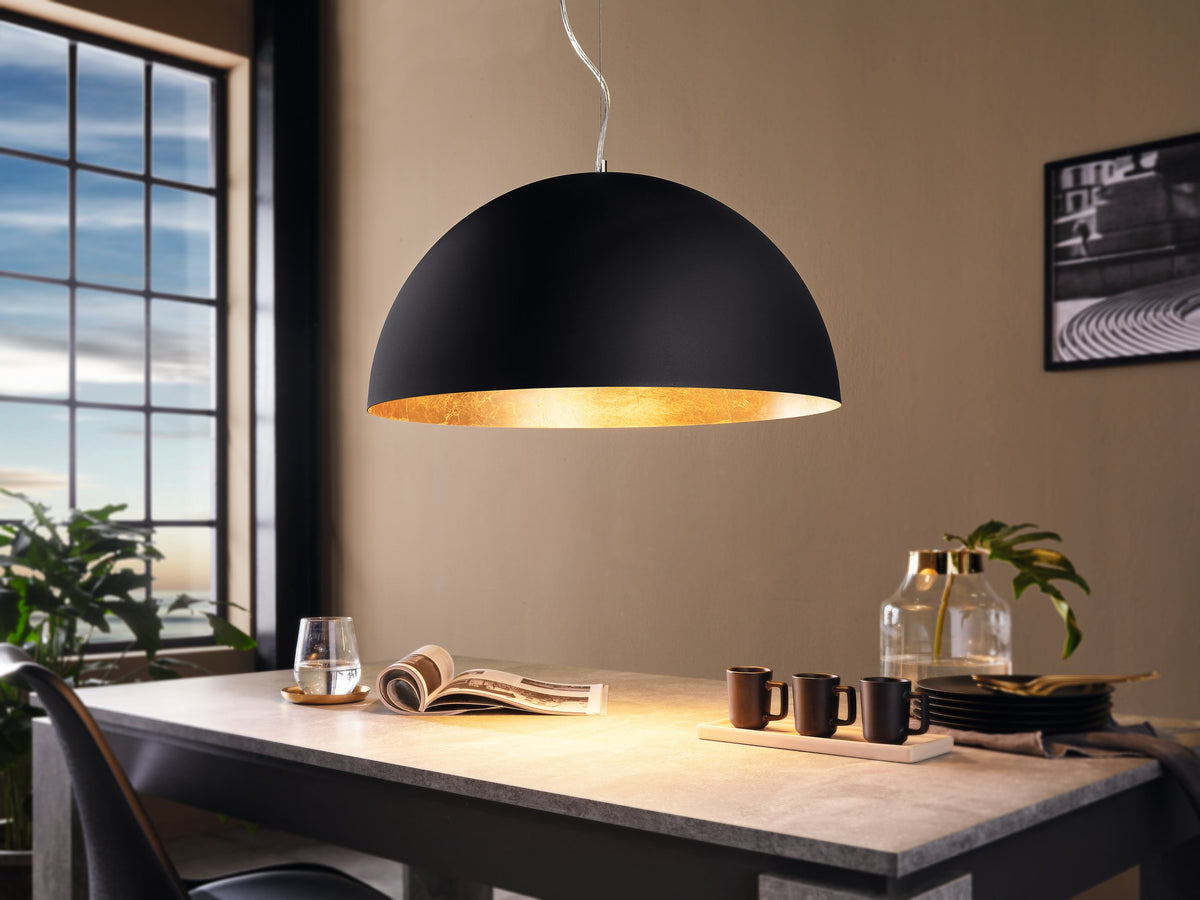 Suspension noire et dorée éclairant une table dressée près d'une fenêtre lumineuse.