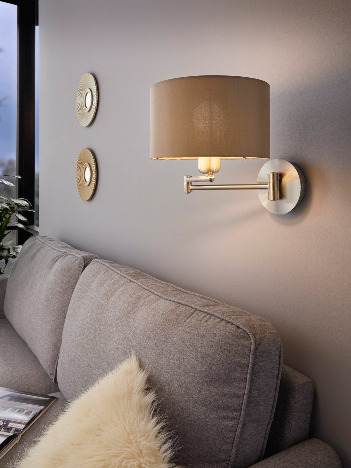Mise en ambiance salon, applique allumée au-dessus d'un canapé gris