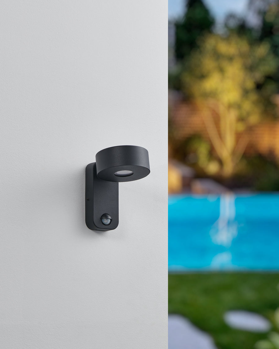 Luminaire mural éteint sur mur blanc, piscine et jardin flous en arrière-plan