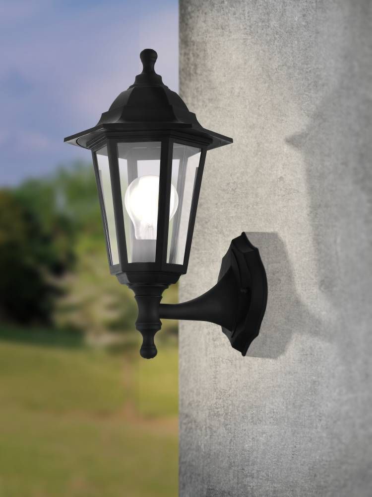 Applique extérieure noire installée sur un mur gris, ampoule allumée, en extérieur.
