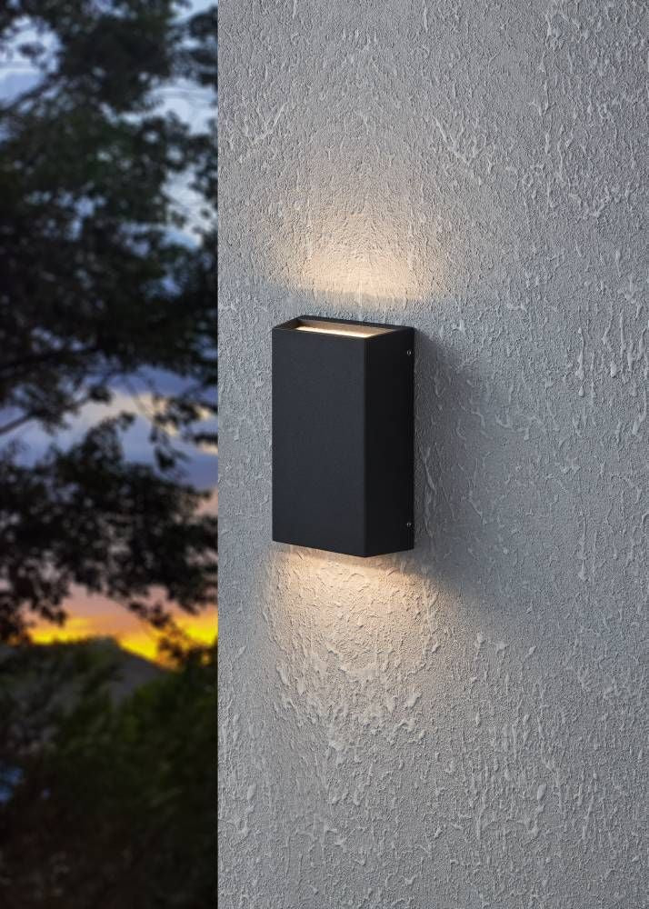 Mise en ambiance : applique murale noire allumée sur façade texturée au crépuscule