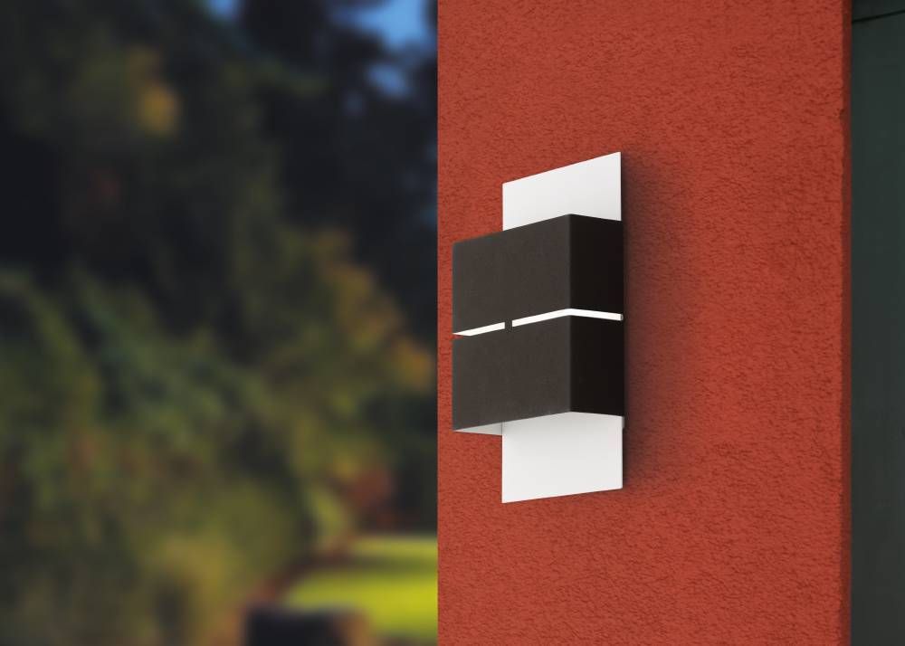 Applique extérieure bicolore sur mur rouge, feuillage flou à l'arrière-plan