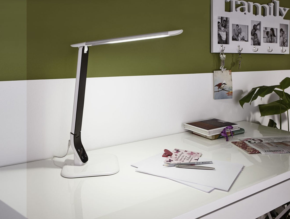 Lampe blanche allumée posée sur un bureau, éclairant des documents et un mur vert.