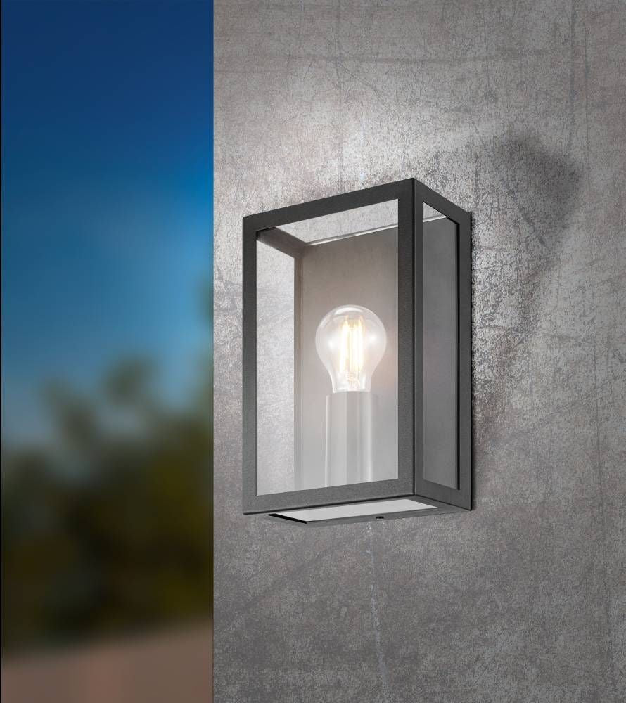 Applique murale noire installée sur un mur gris texturé, ciel bleu en arrière-plan, ampoule allumée