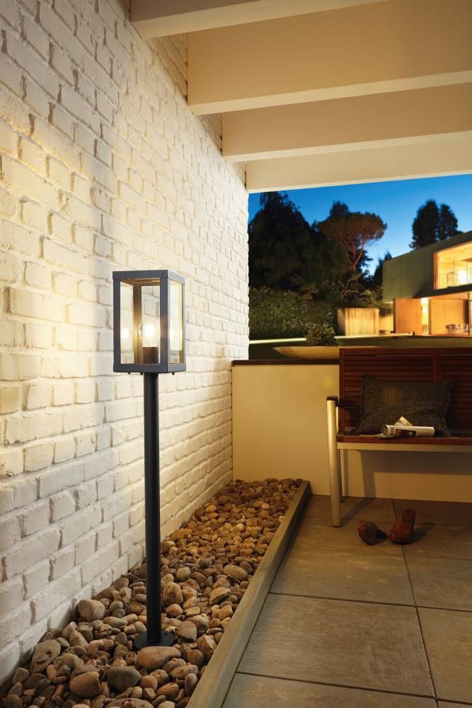 Lampadaire allumé contre mur de briques blanches, terrasse avec galets et banquette au crépuscule.