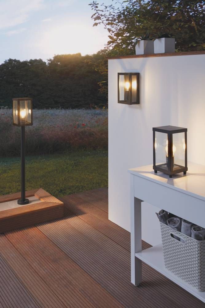 Vue extérieure avec lampadaire, applique murale et lanterne de table allumées sur terrasse.