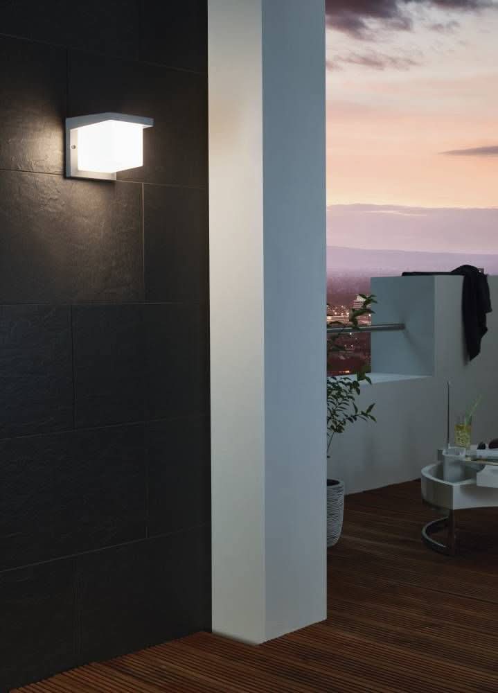 Luminaire mural extérieur anthracite et blanc installé sur un mur sombre, balustrade et vue urbaine.