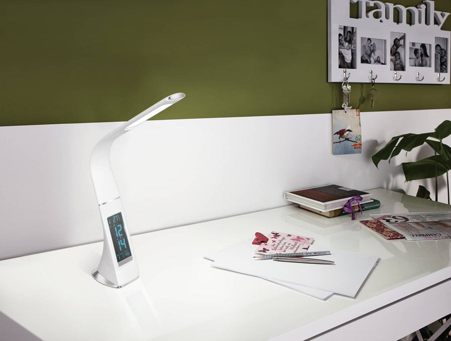 Lampe blanche allumée posée sur un bureau blanc devant un mur vert olive