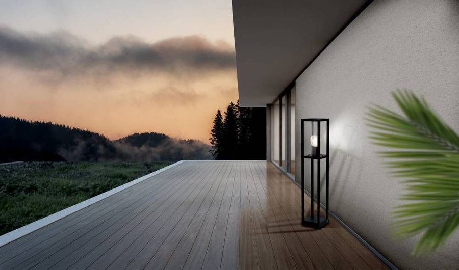 Lampadaire noir allumé contre un mur blanc sur terrasse au crépuscule avec brume