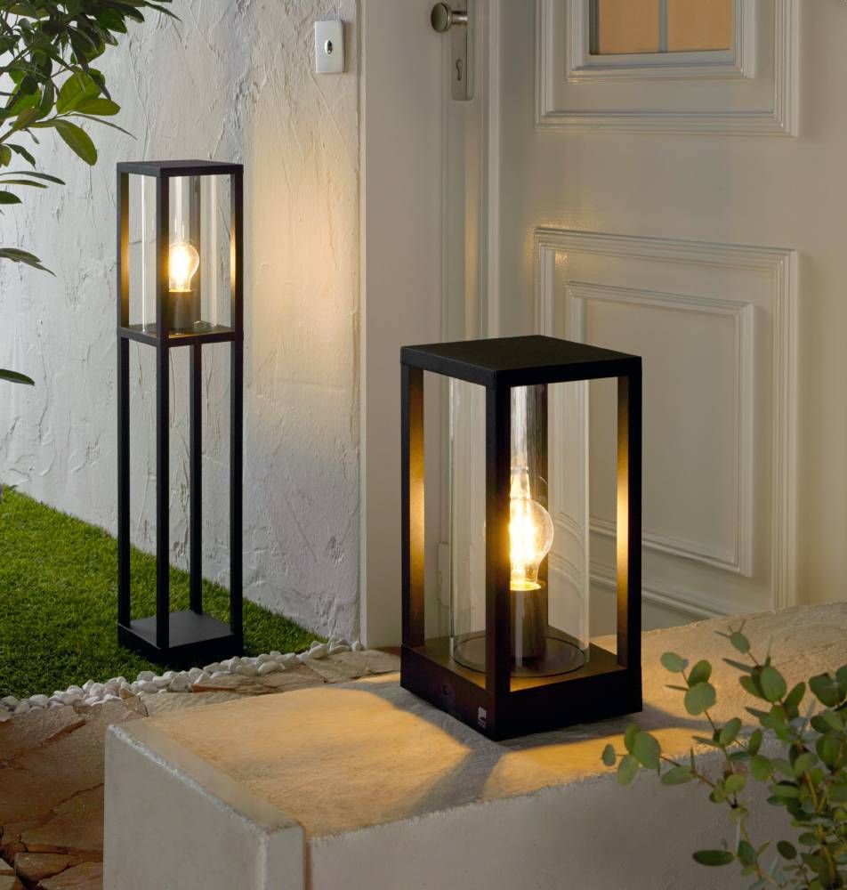 Deux lampes noires rectangulaires allumées devant une porte, l'une haute et l'autre basse