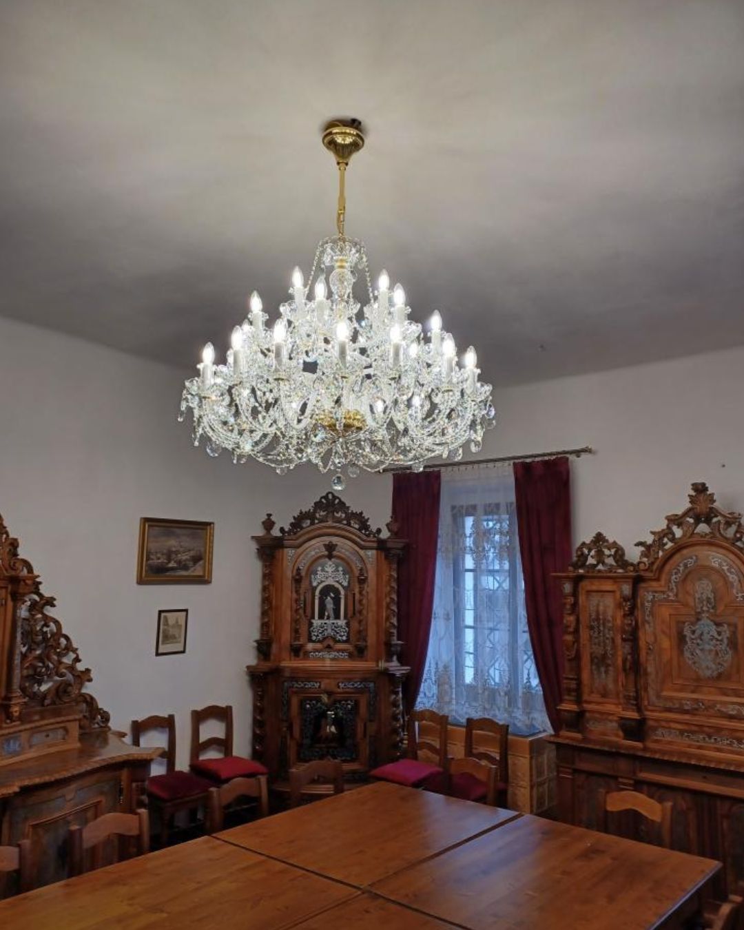 Lustre allumé éclairant une salle à manger aux meubles anciens en bois sculpté