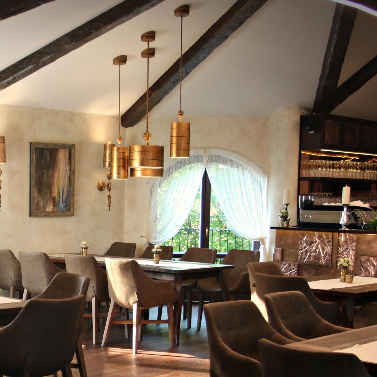Mise en ambiance dans un restaurant rustique avec plusieurs suspensions dorées au-dessus des tables.