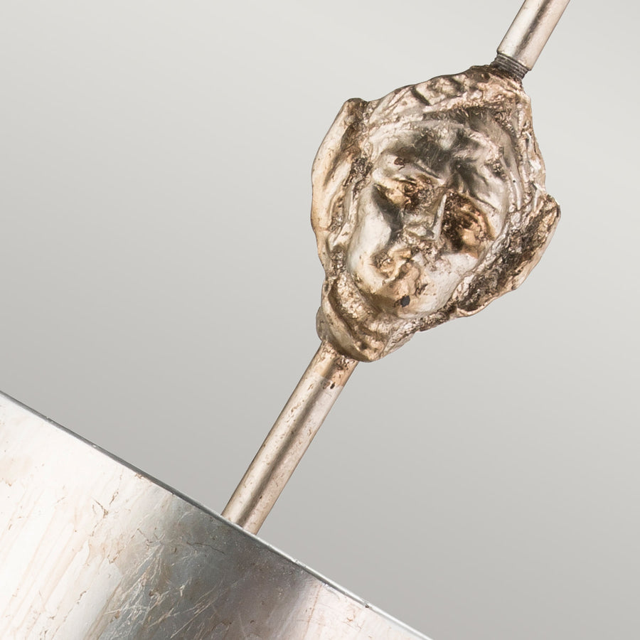 Gros plan sur le masque doré sculpté qui orne la tige de la suspension