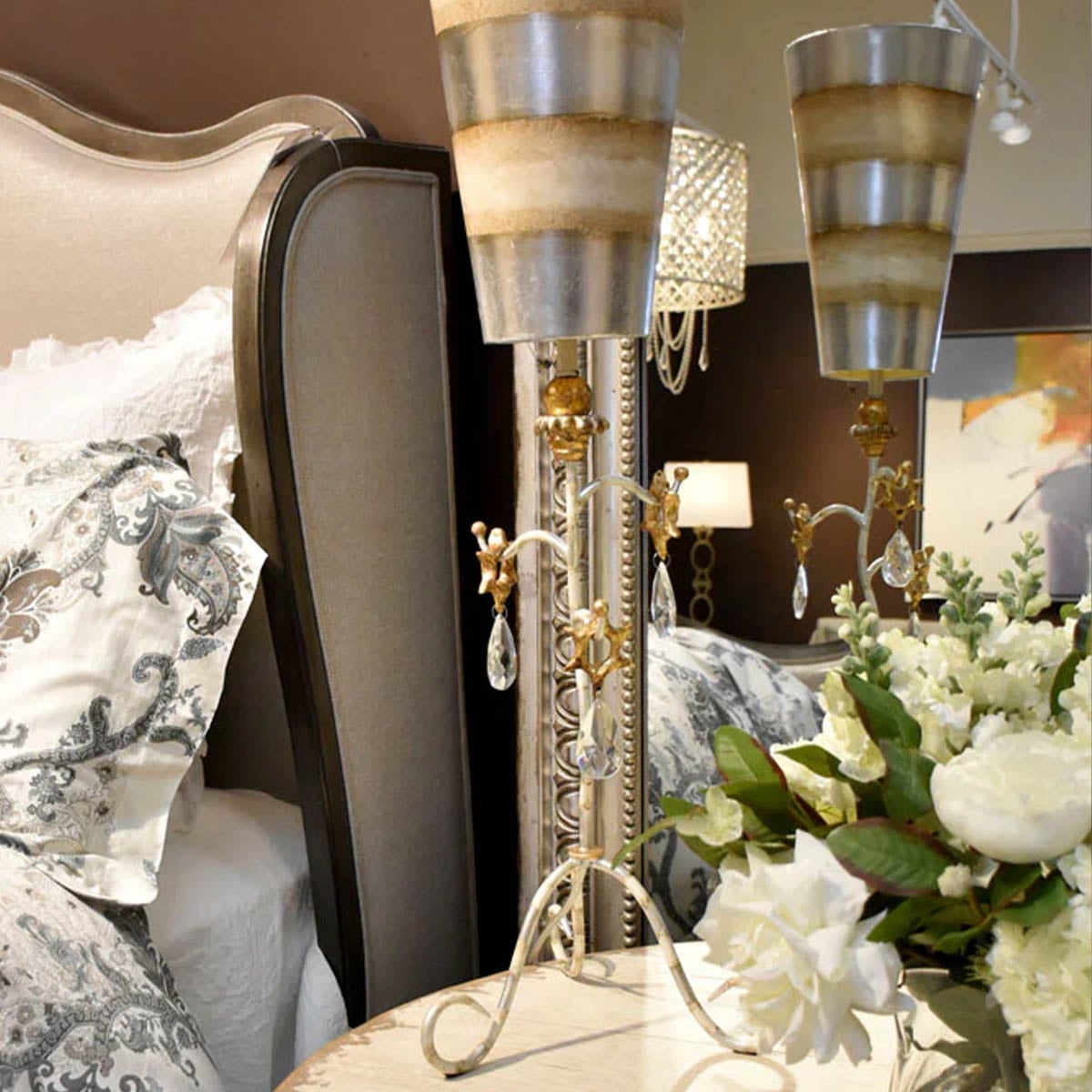 Lampe à poser sur chevet près d'un lit et de fleurs blanches.