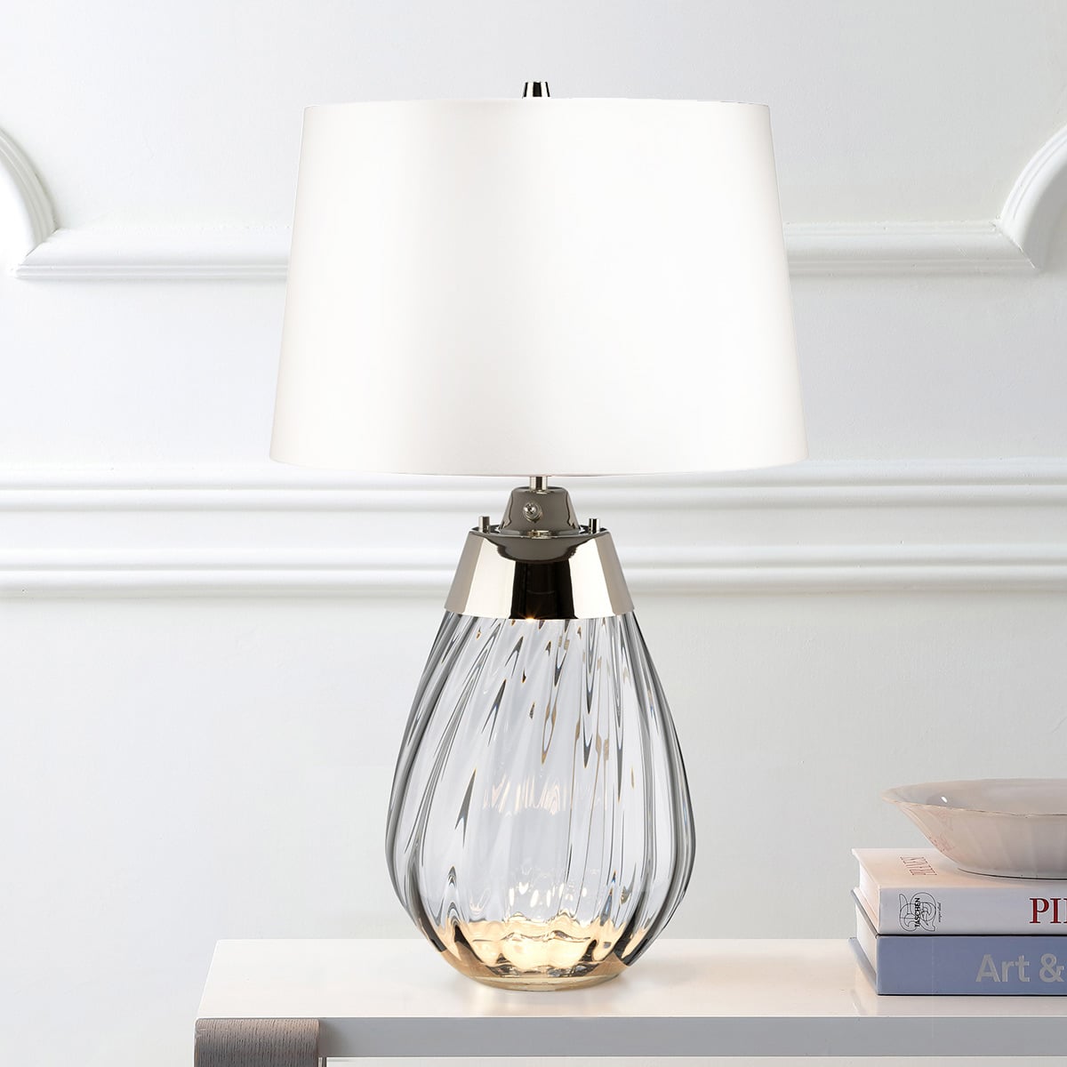 Mise en ambiance de la lampe posée sur une console blanche devant un mur mouluré