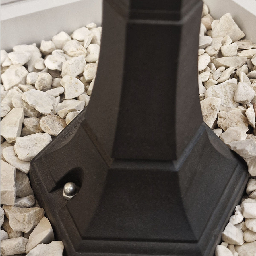 Détail de la base hexagonale noire vissée, posée sur des graviers clairs