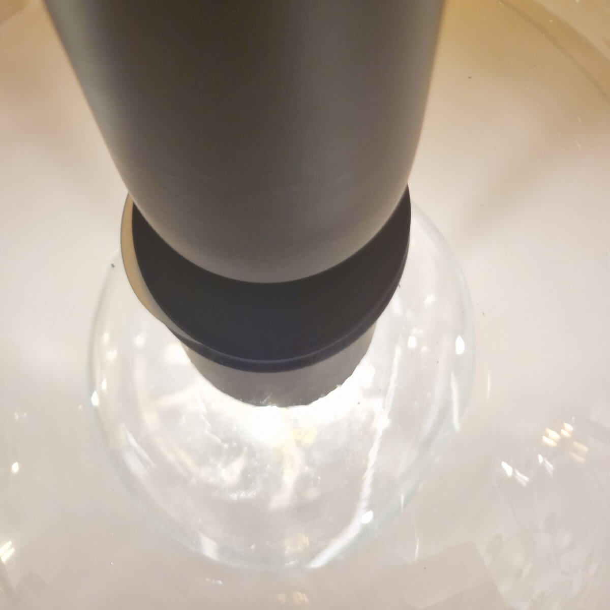 Détail rapproché de la douille noire insérée dans l'abat-jour en verre clair.