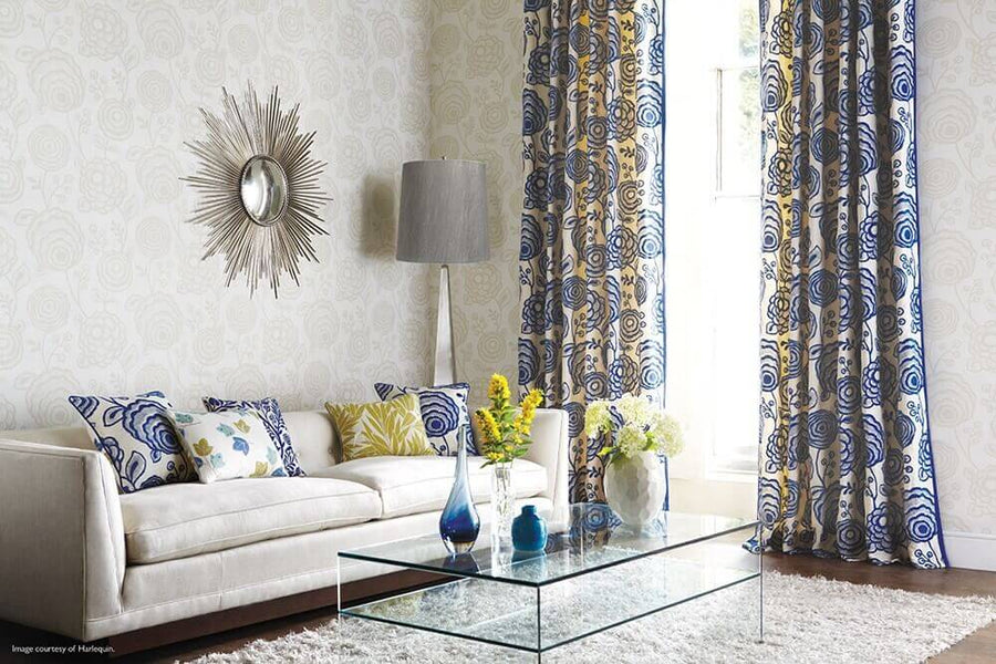 Lampadaire allumé dans un salon, près d'un canapé blanc, miroir soleil et rideaux fleuris.
