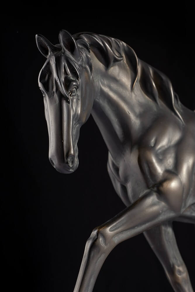 Gros plan sur la tête du cheval en bronze, crinière et muscles détaillés sur fond noir.