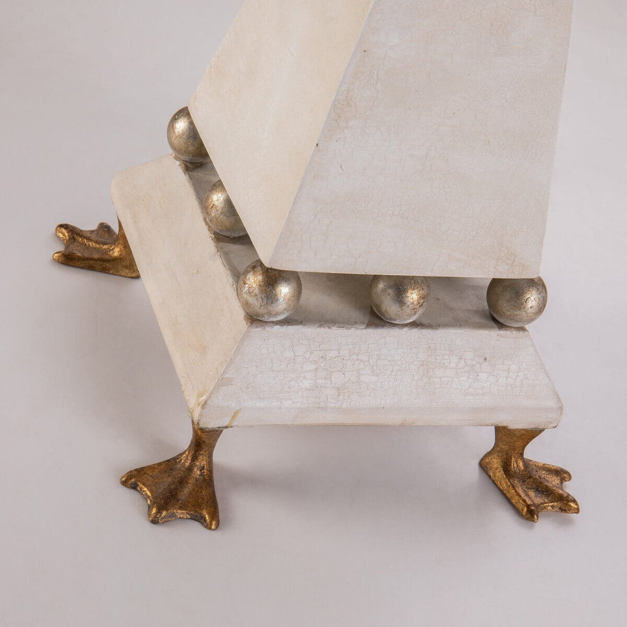Détail du socle crème, des boules argentées et des pieds dorés en forme de pattes.