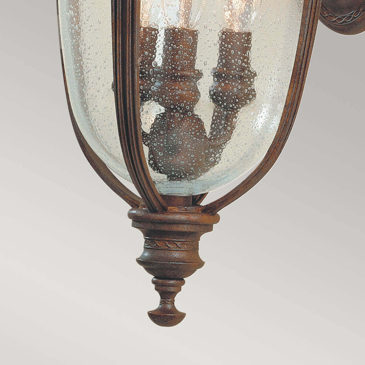 Gros plan sur le bas de la lanterne, verre bullé et finial bronze ouvragé suspendu.