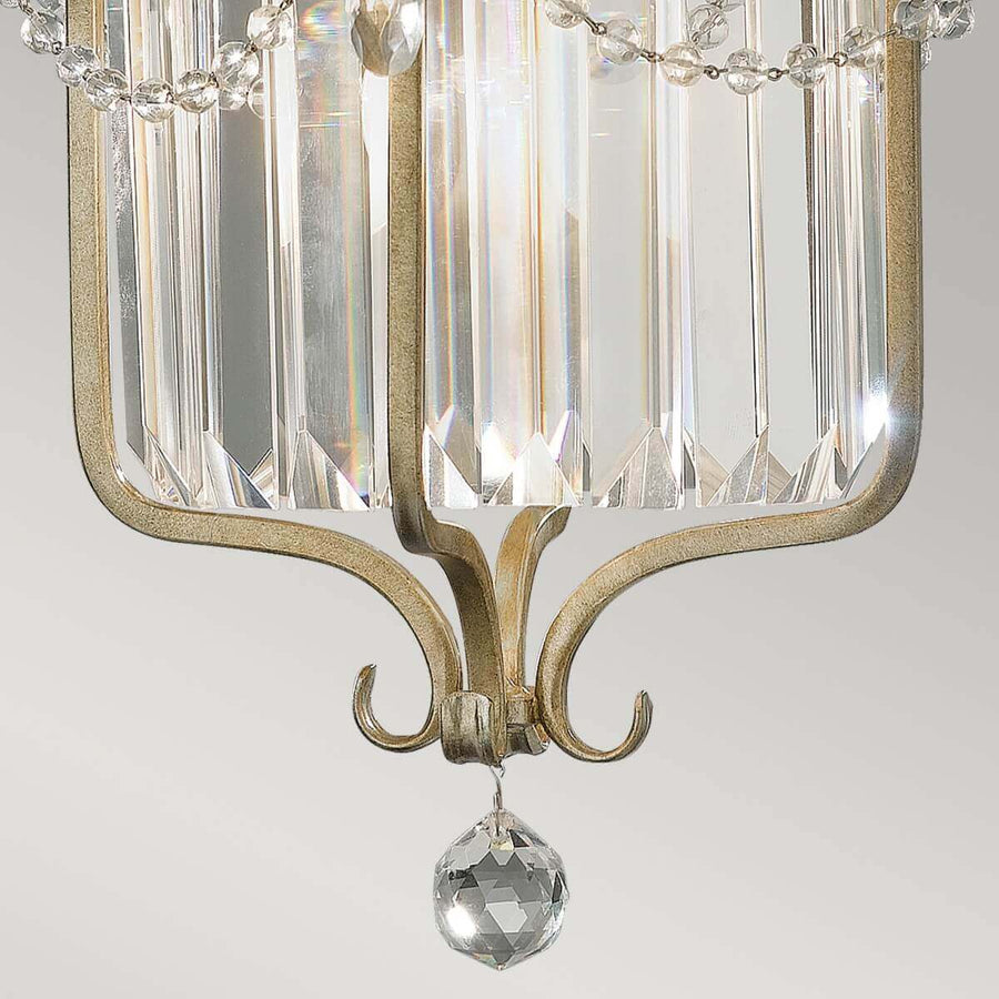 Détail du bas : boule de cristal facettée suspendue sous les volutes métalliques dorées et argentées.