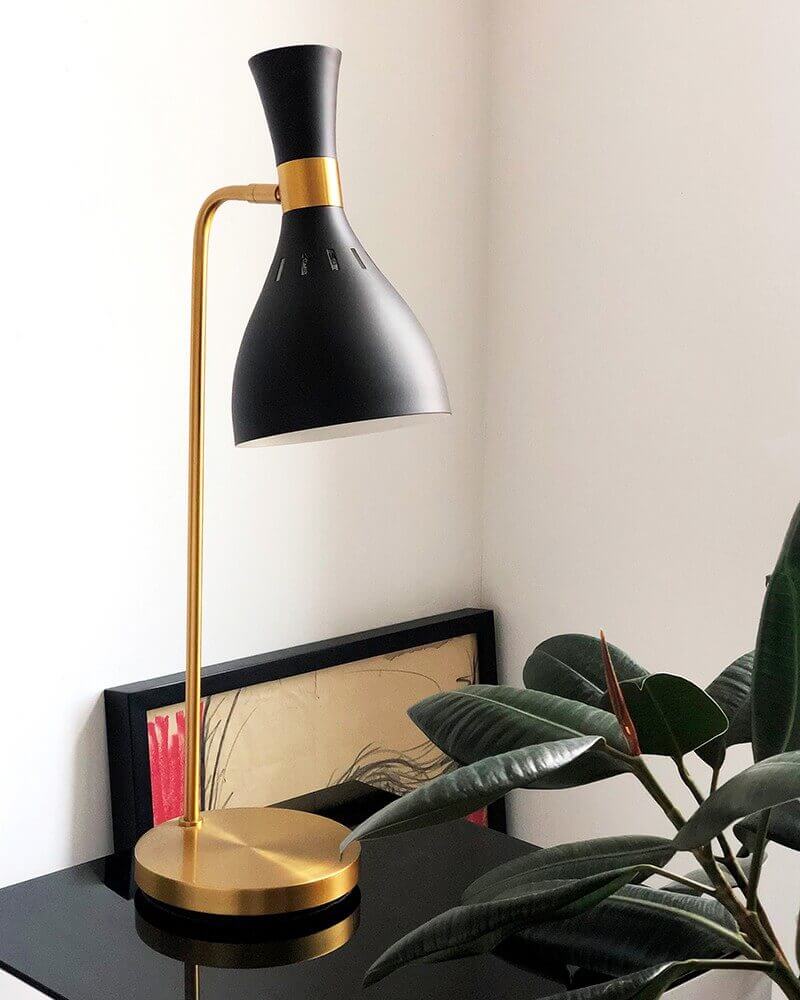 Lampe noire et dorée allumée posée sur une table noire avec plante