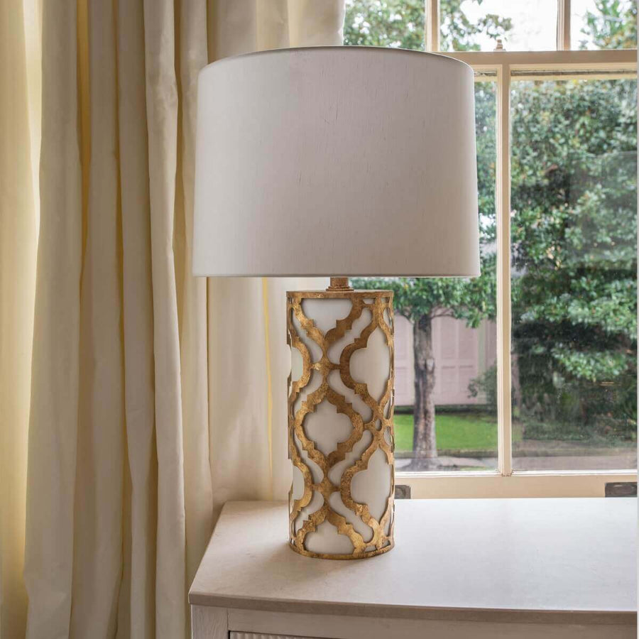 Lampe à poser dorée et blanche posée sur un meuble devant une fenêtre