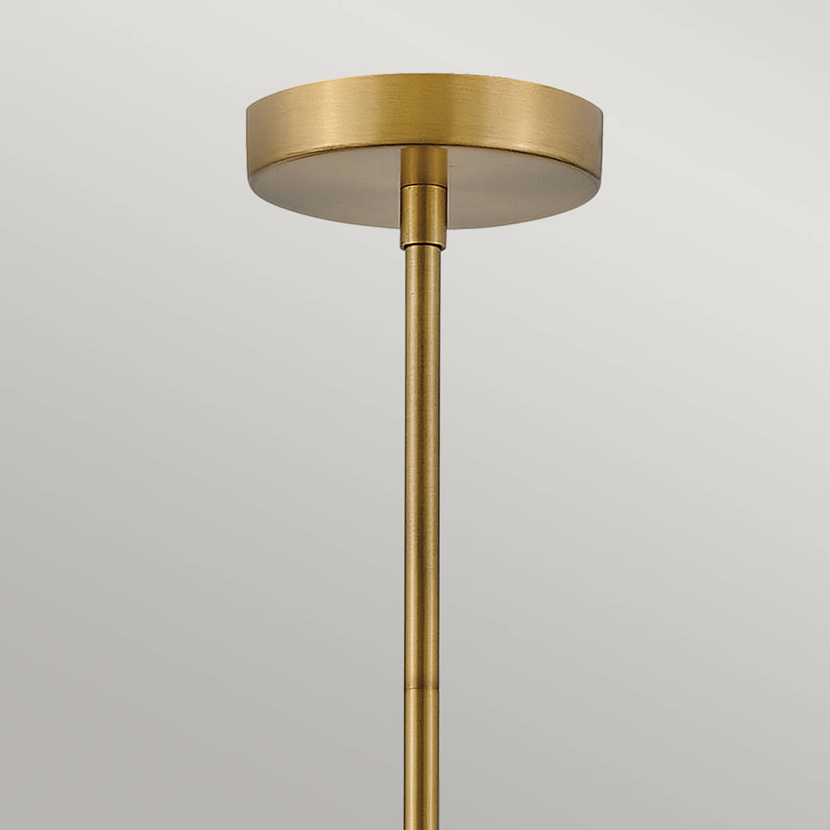Rosace ronde en laiton fixée au plafond et tige dorée verticale.