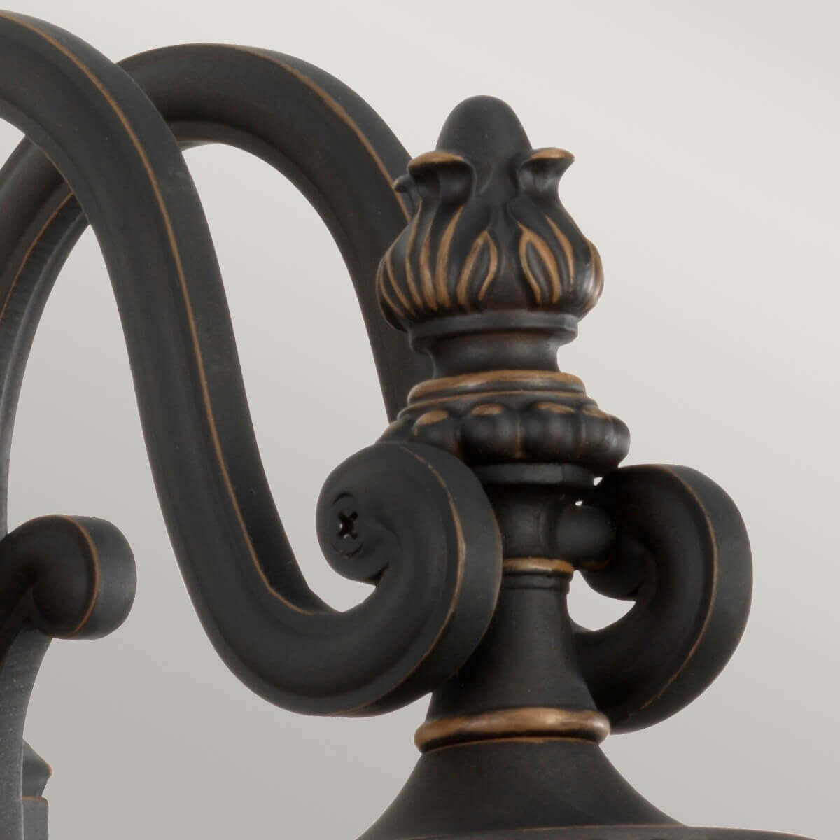 Détail du fleuron sommital et des volutes en bronze patiné aux reflets dorés.