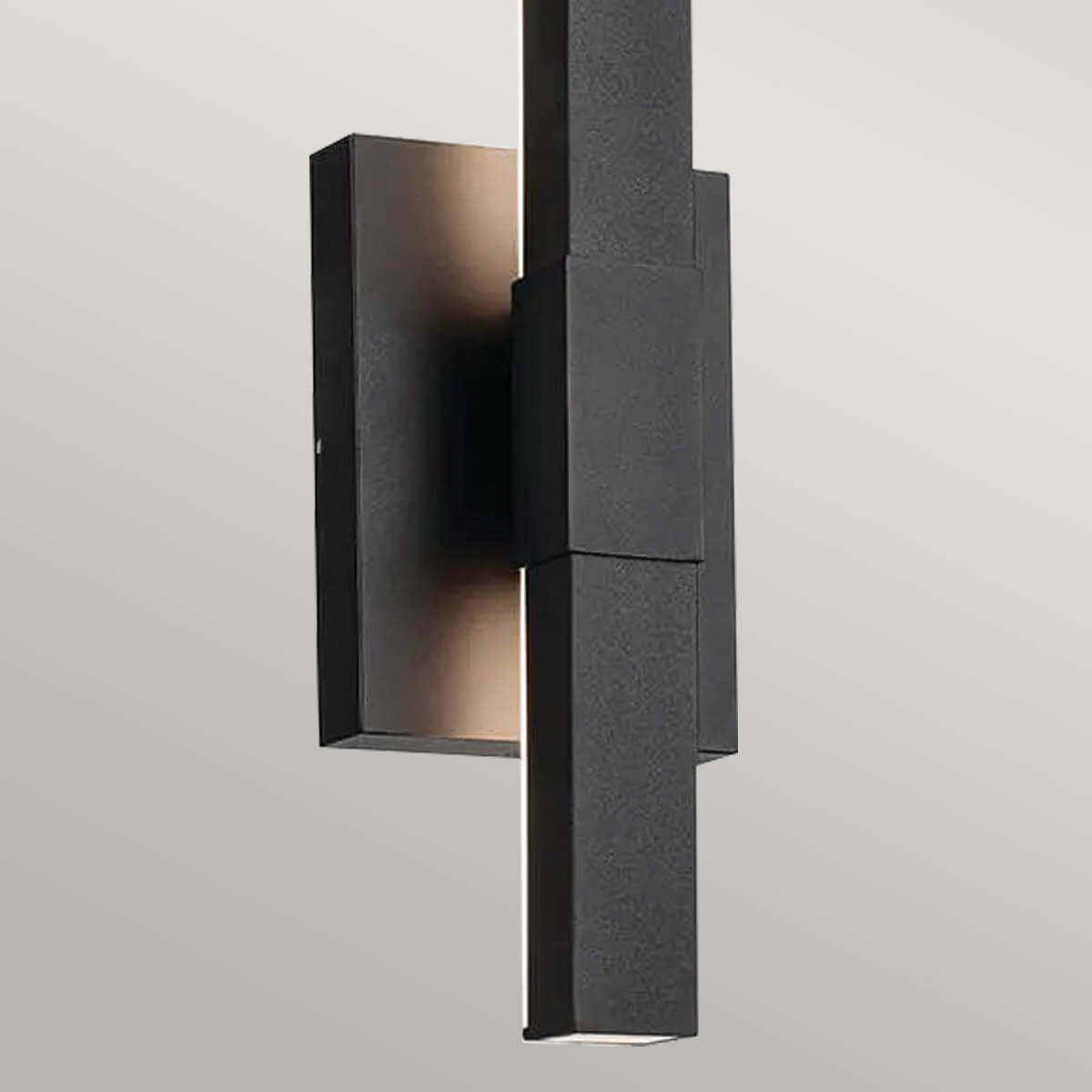 Détail du centre de l'applique noire, platine et jonction verticale éclairées en lumière chaude.