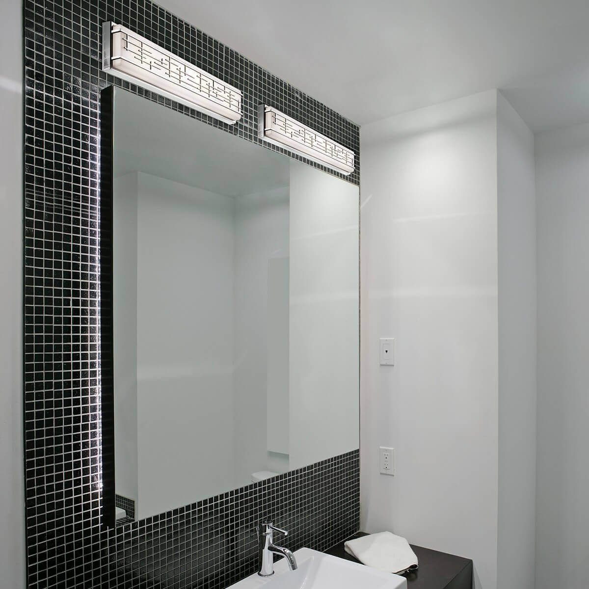Mise en ambiance salle de bain, deux appliques chromées fixées au-dessus d'un grand miroir sur mosaïque noire