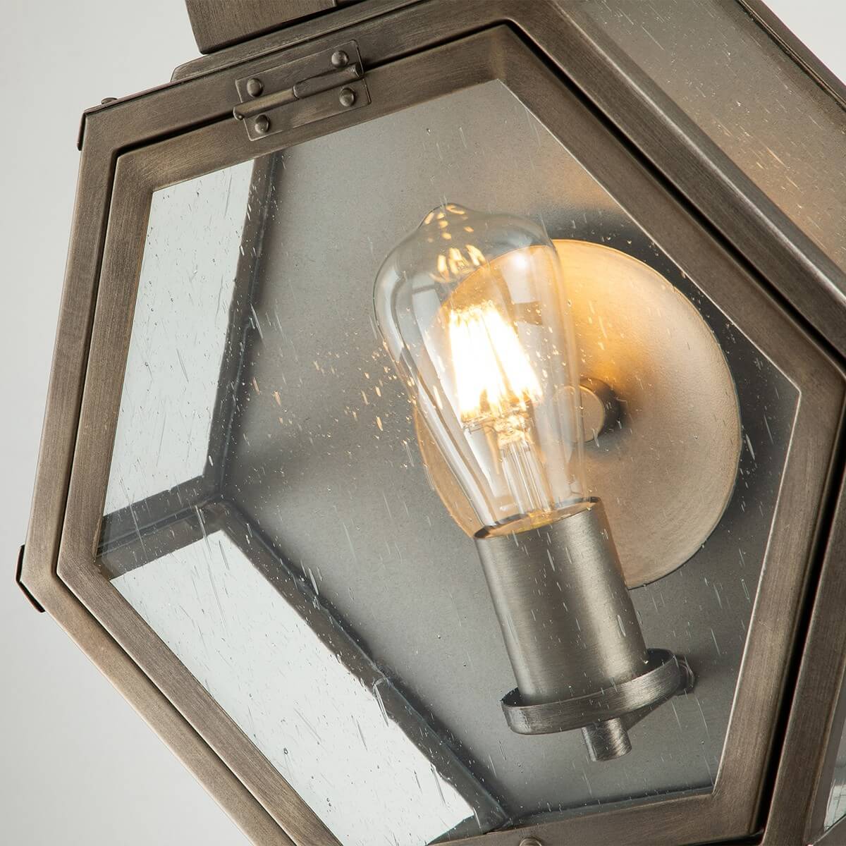 Gros plan à travers le verre grenu montrant l’ampoule à filament allumée et le support.