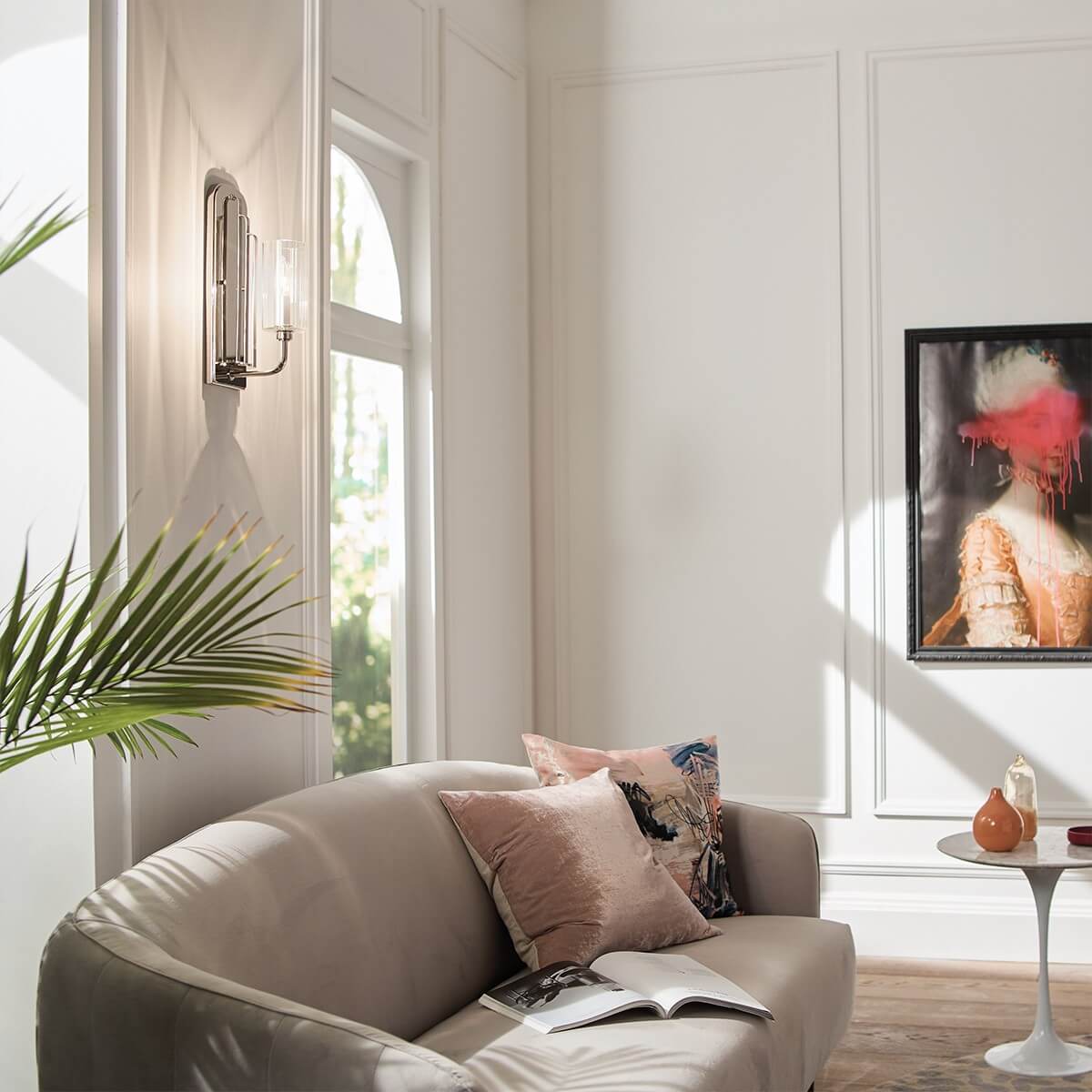 Mise en ambiance : applique allumée sur un mur blanc, canapé, tableau et plante verte.