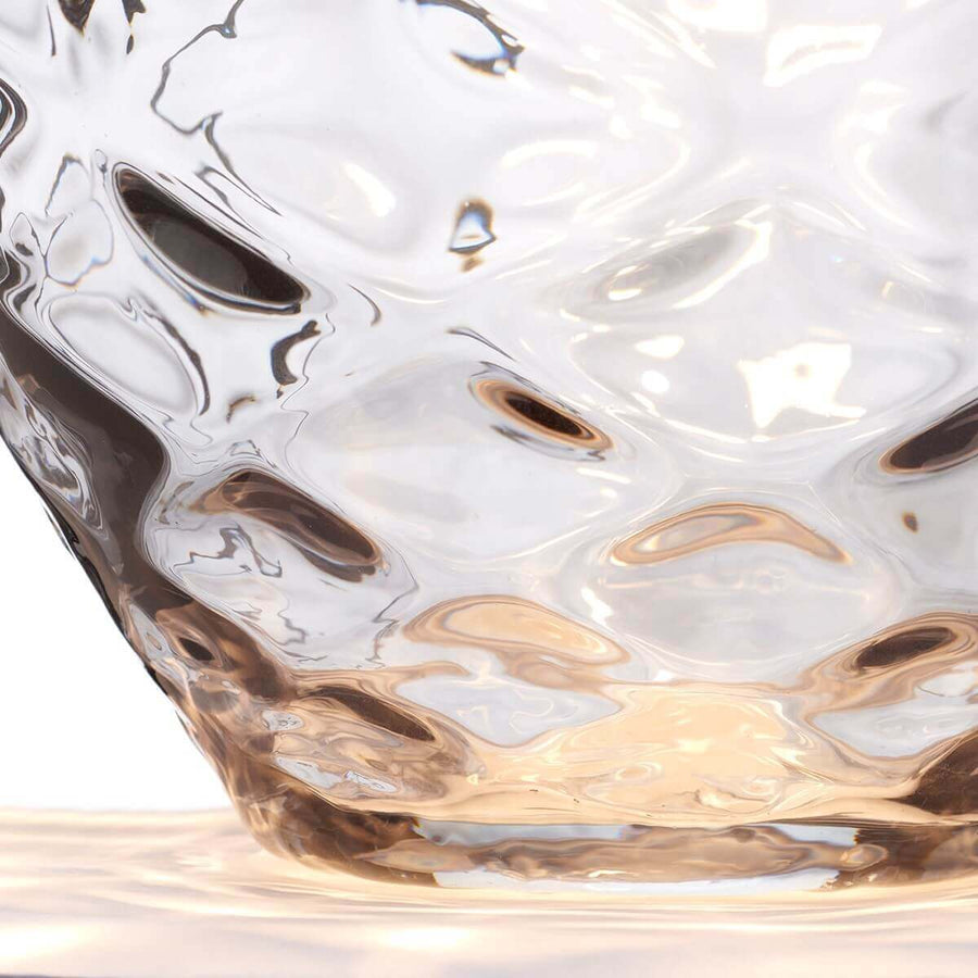 Gros plan sur la texture martelée du verre et ses reflets ambrés